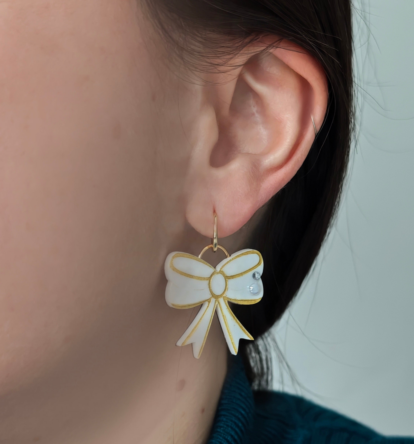 Close-up of an ear wearing a bow-shaped earring with a white center and gold outline.