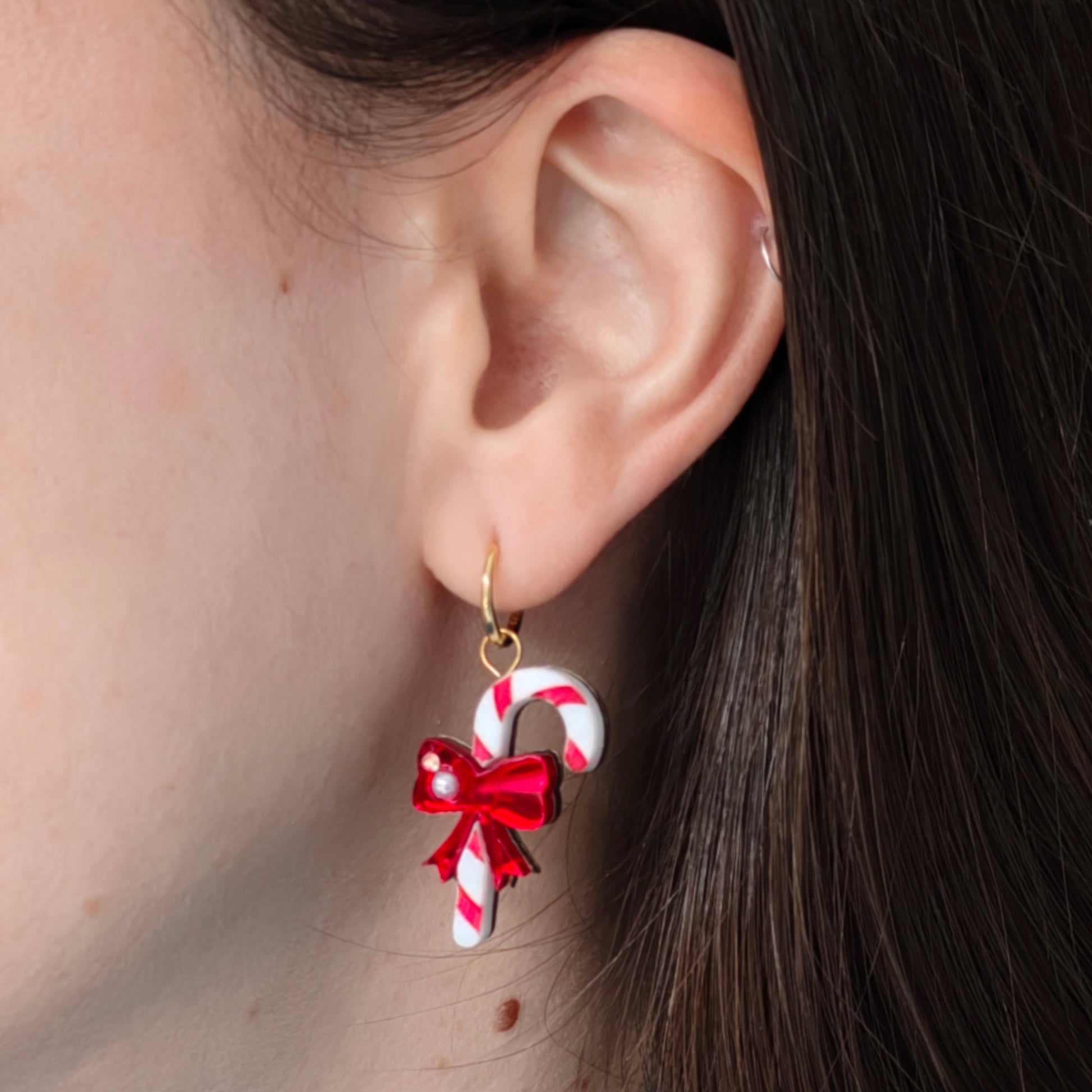 Earring with candy cane and bow design worn by a person