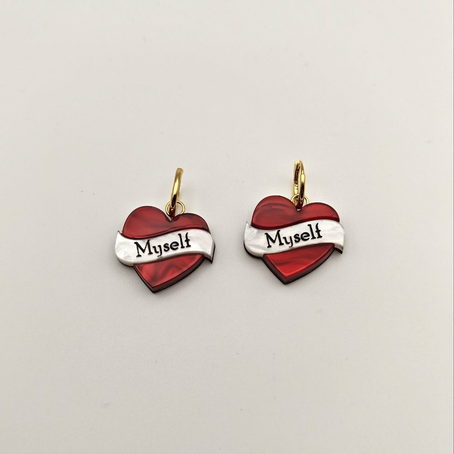 Heart-shaped earrings hoop charm with 'Myself' text on a light gray background