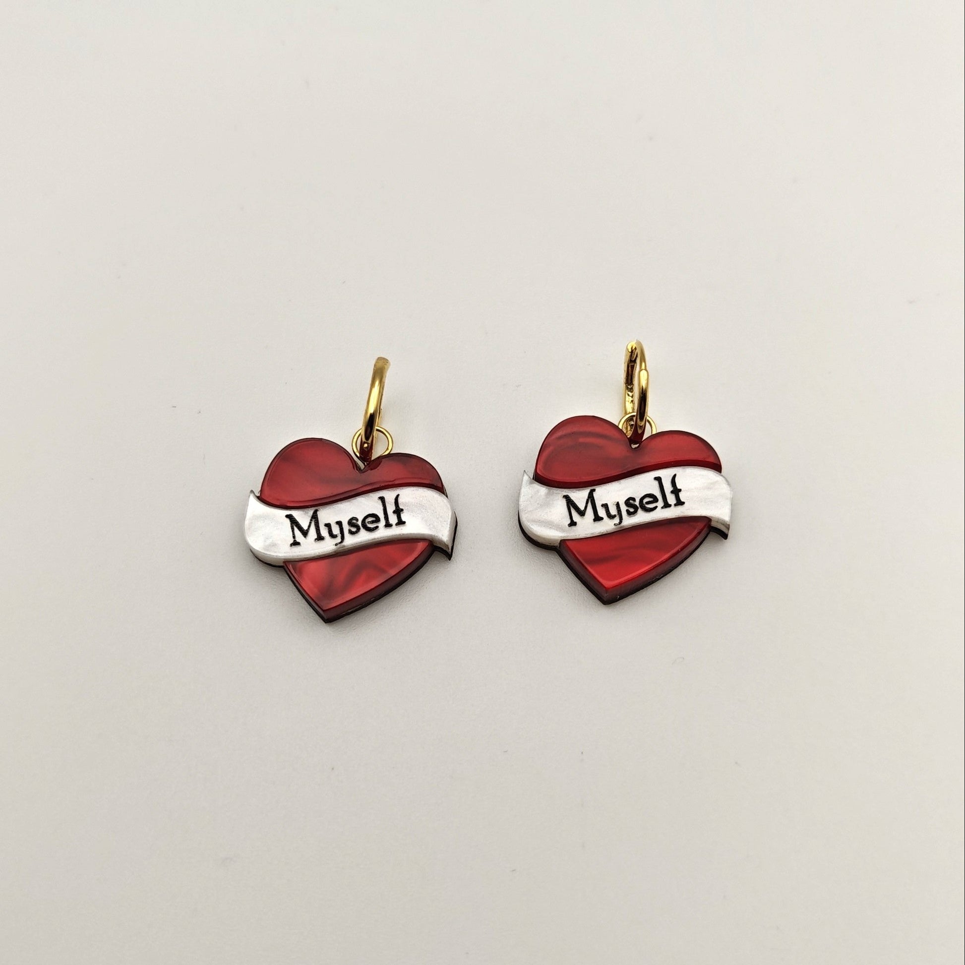 Heart-shaped earrings hoop charm with 'Myself' text on a light gray background