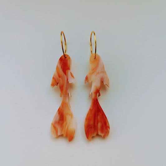 Pair of orange and white marbled fish-shaped earrings (Koi) on a light gray background